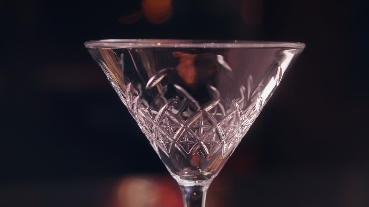 Primo piano di un barista che versa un cocktail rosa sour con schiuma in un bicchiere a coppa in un'elegante ambientazione da bar.