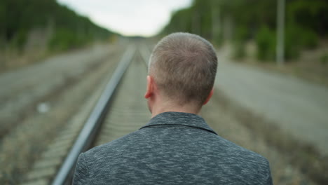 a head view of an aged man walking alone on a railway track, looking his left side, looking around with bokeh view of trees and electric poles