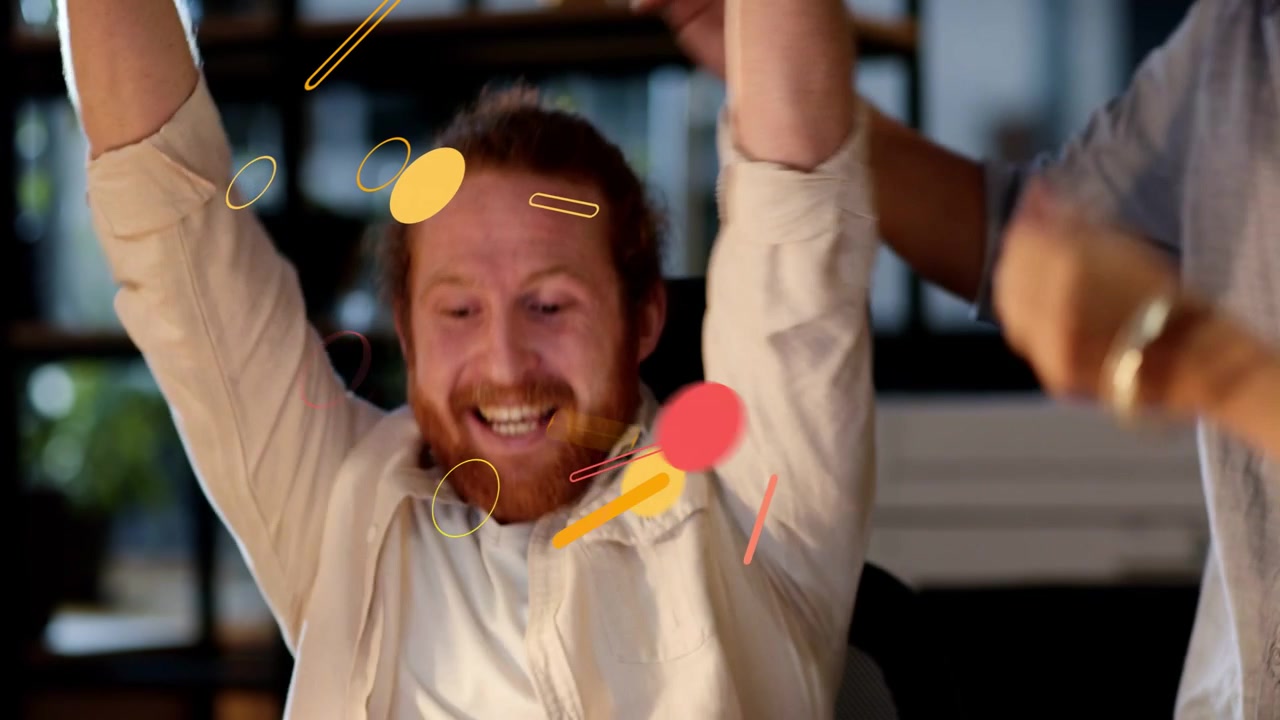 Seated man reacting to confetti and coworker leaning in, cheering office project win with highfives