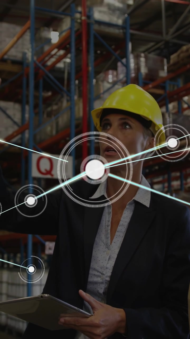 Video verticale: Un caposquadra con elmetto di sicurezza usa un tablet, indicando un display HUD che collega le scaffalature per le operazioni di magazzino.