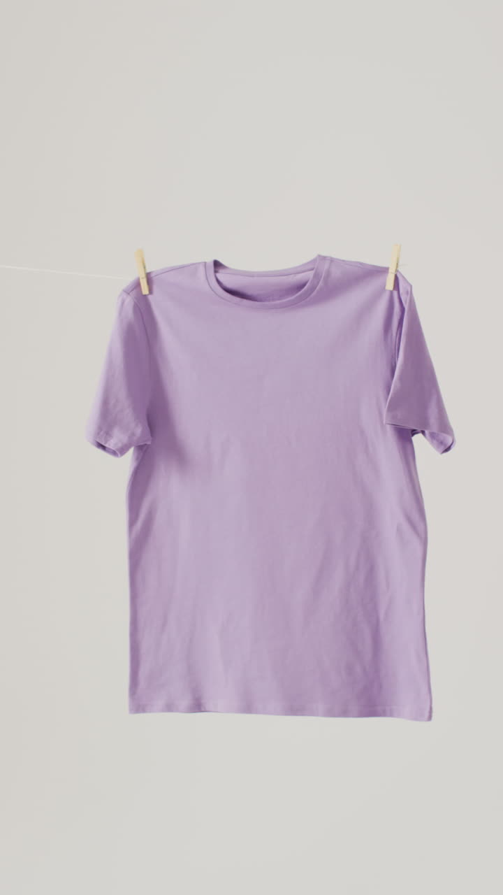 Vertical video of close up of purple t shirt hanging on white background with copy space