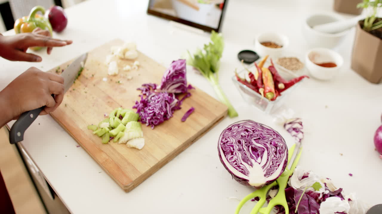 African American woman is chopping vegetables on a wooden cutting board at home