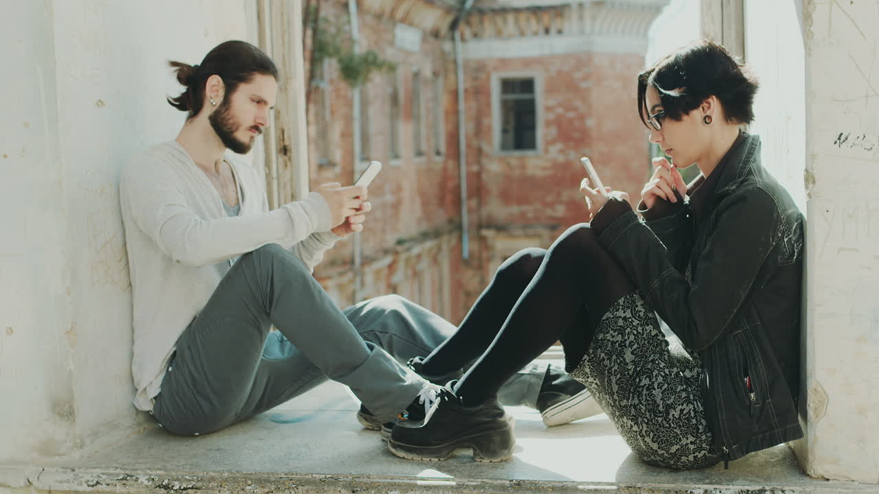 joven hipster pareja sentada en la ventana usa el concepto de teléfonos móviles - la falta de comunicación en vivo