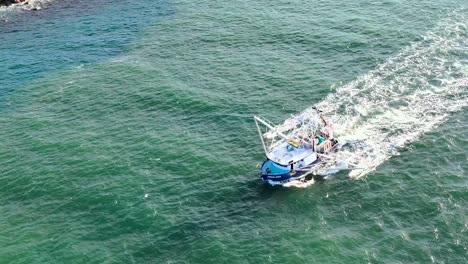 a fishing vessel moves through clear coastal waters, leaving a trail of waves behind.