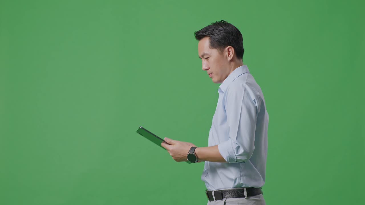 스튜디오에서 녹색 화면 배경에서 는 동안 태블릿을 사용하는 아시아 사업가의 측면 시각