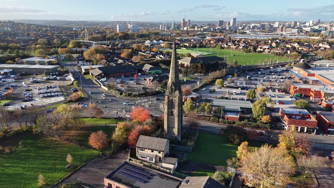 Aerial drone view of historic church spire in Hedge End, Hampshire, surrounded by town streets, residential and commercial buildings, green spaces, autumn trees, and clear daylight