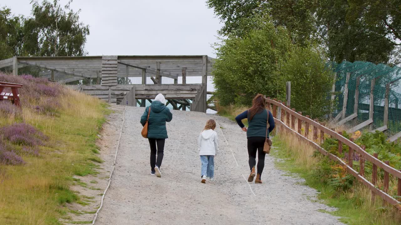 Two adults and child walk uphill on gravel path, overcast day, surrounded by heather