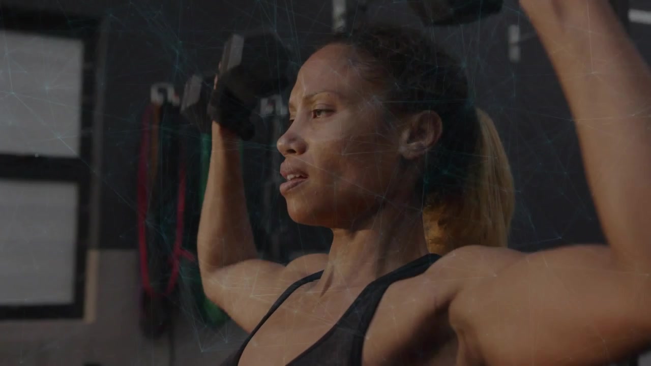 Woman lowering and pressing dumbbells from overhead hold in gym, building shoulder strength