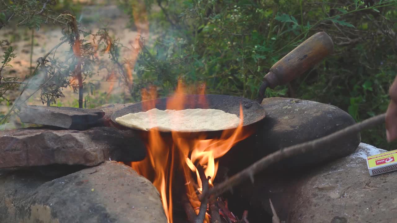 Vista laterale di cucina indiana all'aperto sulle fiamme di un falò nella natura, India