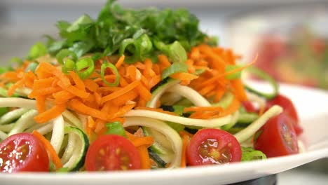 close up shot of zucchini noodles garnished with cilantro shredded carrots spiralizer to make zucchini noodles zoodles adding to bowl healthy vegan vegetarian lifestyle diet detox