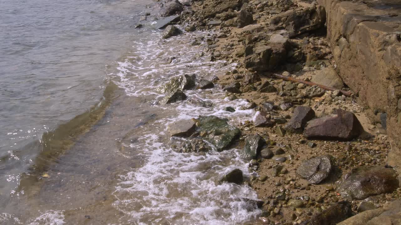 toma amplia de pequeñas olas ondeando contra una playa rocosa en un día soleado