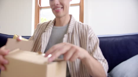 hombre biracial excitado abriendo una entrega en una caja de cartón, cámara lenta