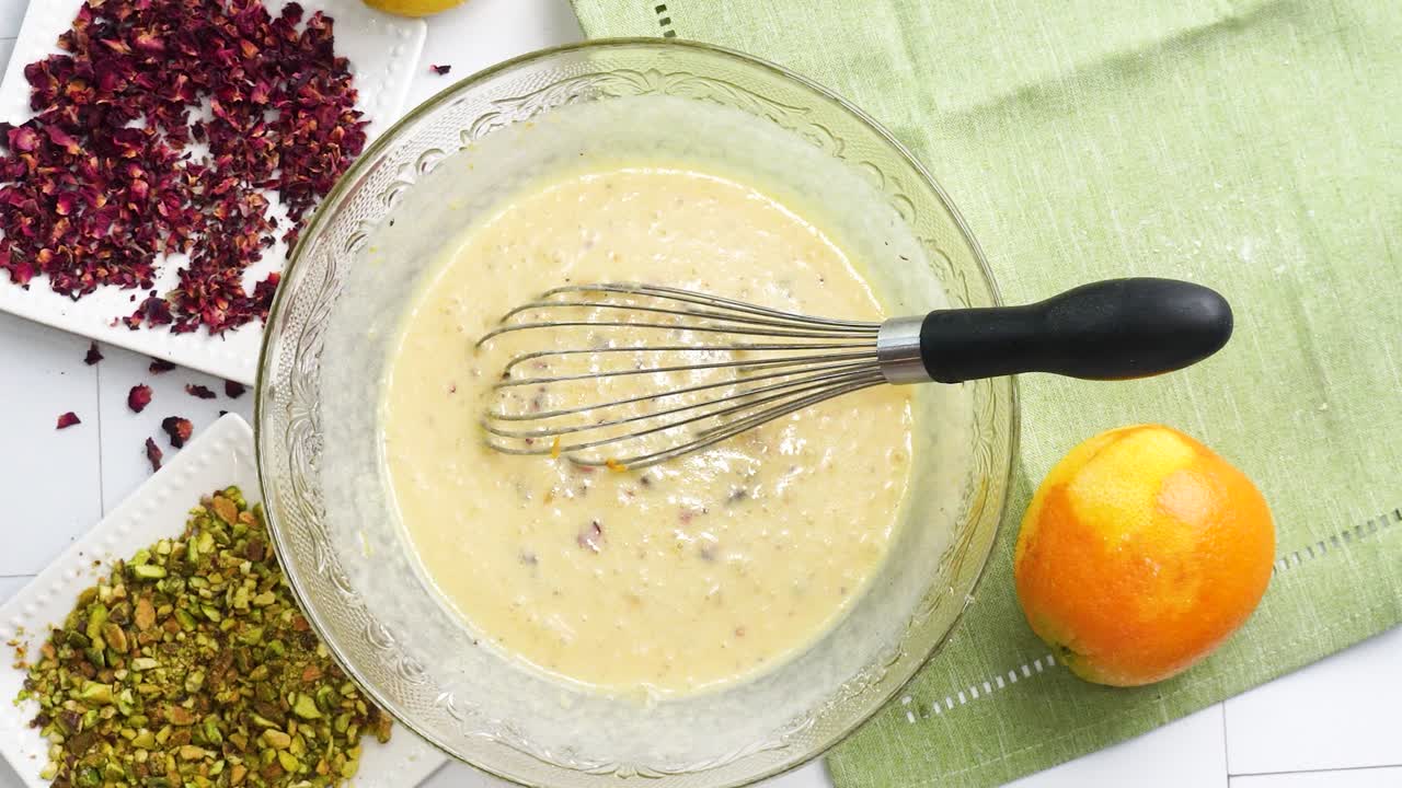 Baking a dessert called Persian Love Cake made with rose petals and pistachios. Cake with white glaze frosting. Mixing in flour mixture. Beautiful cake for tea and coffee time or a celebration