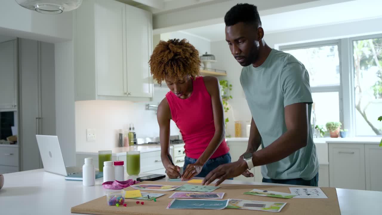 Couple leaning over wooden board, starting planning in kitchen, arranging printed sheets for craft