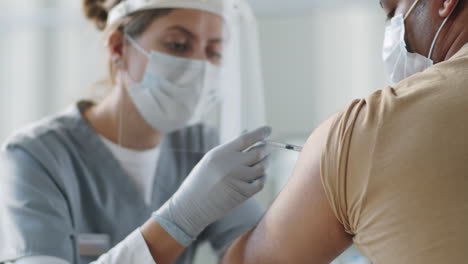 female doctor in protective uniform giving vaccine to patient