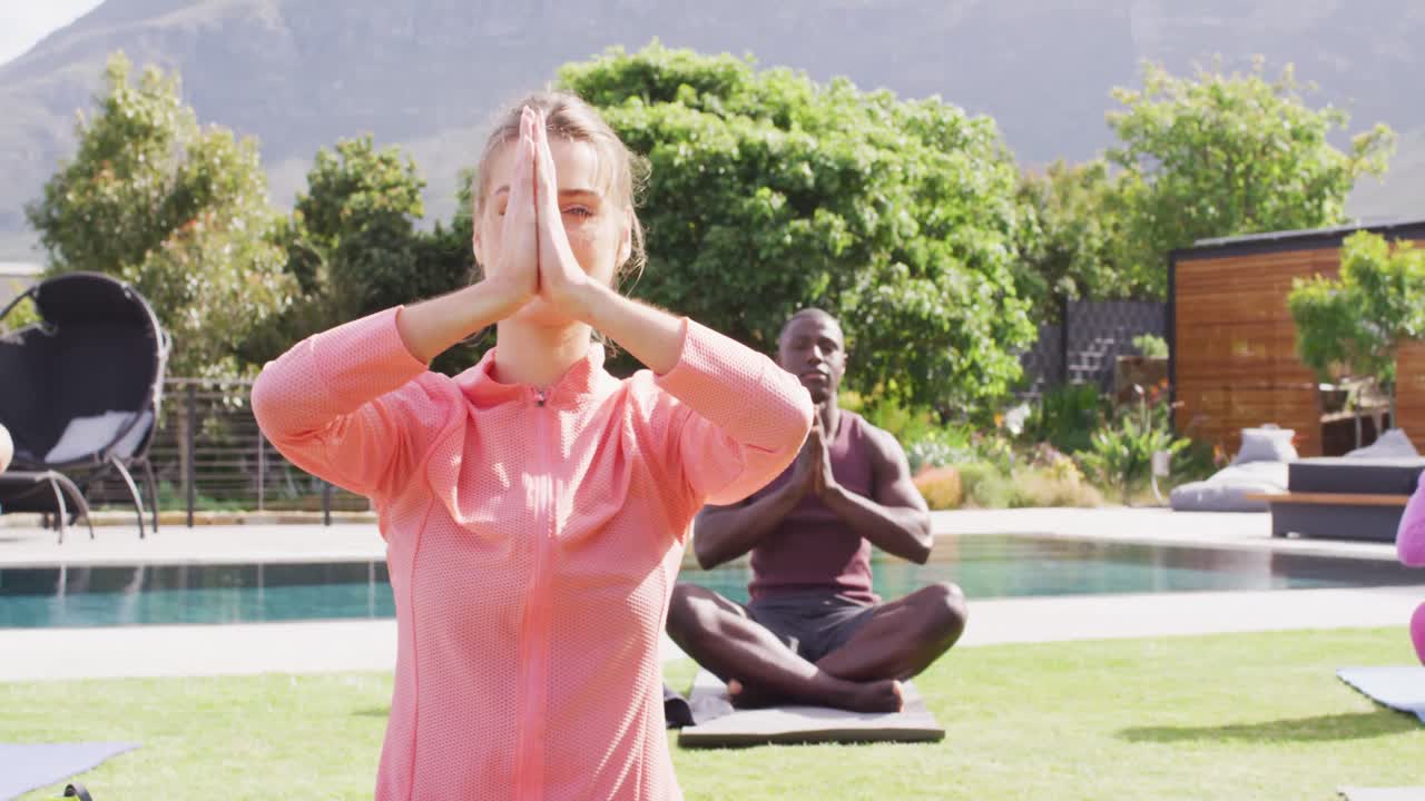 Gruppo felice di amici di diverse etnie che praticano yoga e meditano in giardino.