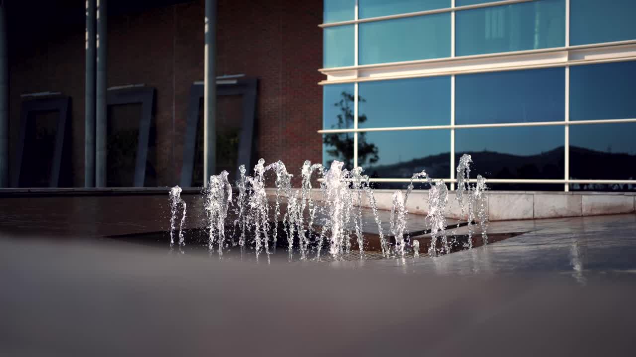 Toma estática de agua salpicando de una fuente frente a un edificio moderno acristalado