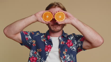 handsome tourist man putting half of oranges on eyes, vegetarian lifestyle, vitamins for health