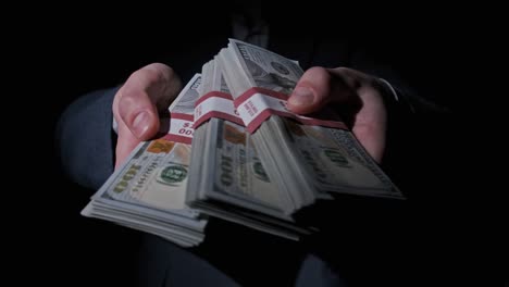 businessman in suit shows stack of 10000 american dollars on black background