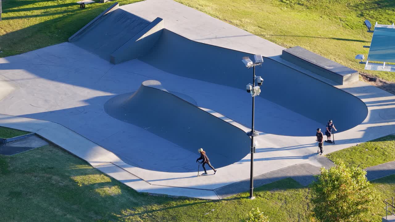 Children skateboarding and riding scooters in a sunlit skate park bowl, showcasing dynamic movement and youthful energy