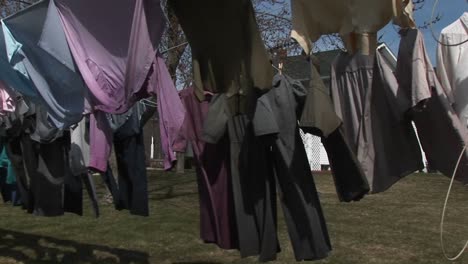 colorful shirts and dark dresses hang on a clothesline to dry in wind