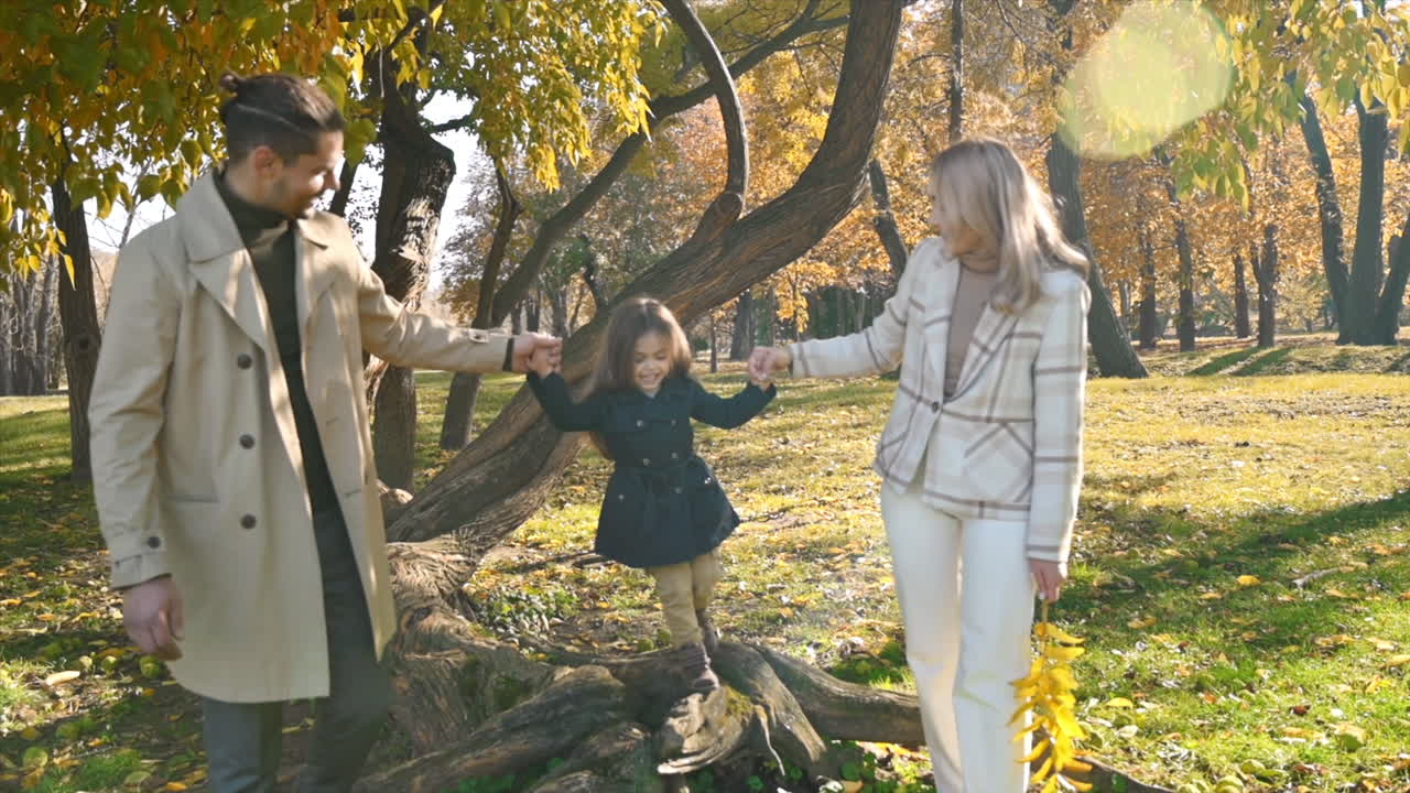Happy family in an autumn park. Mother and father playing and walking with daughter, yellowed trees around. Slow motion
