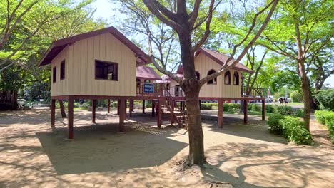 un tranquilo patio de recreo en el parque rama 9 de bangkok, con cabañas elevadas bajo árboles exuberantes en un día soleado