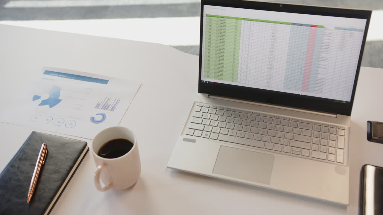 Working from home, laptop displaying spreadsheet next to coffee cup and documents
