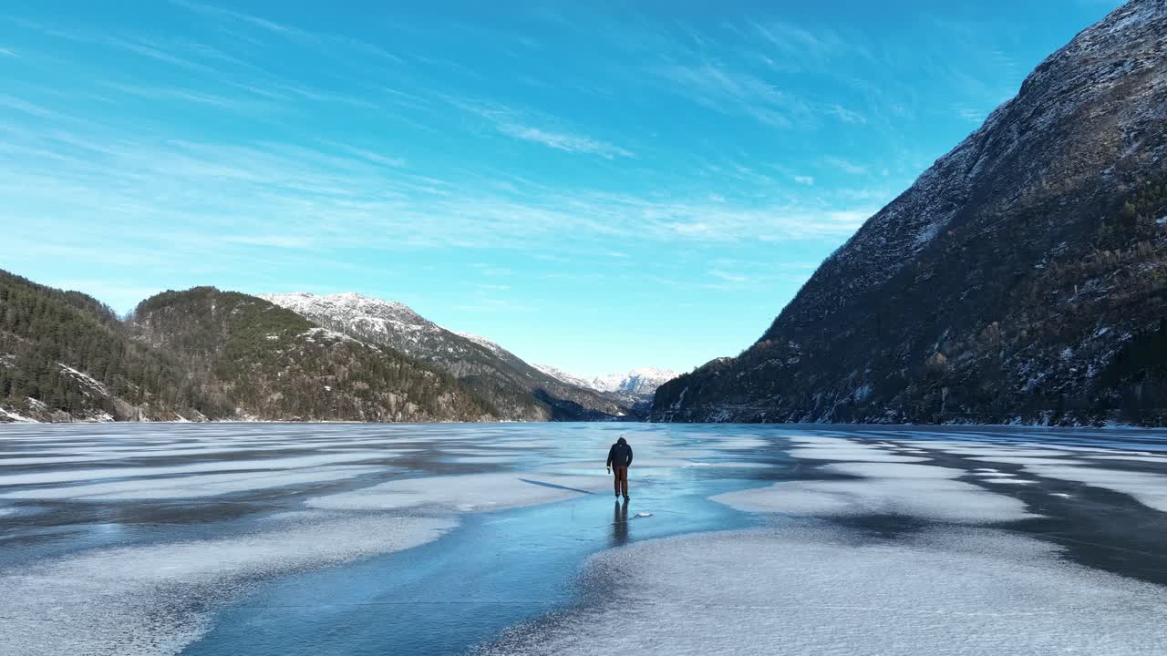 Luftfoto følger skøyteløper på frossen norsk fjord, isdans på klar morgen under strålende blå himmel
