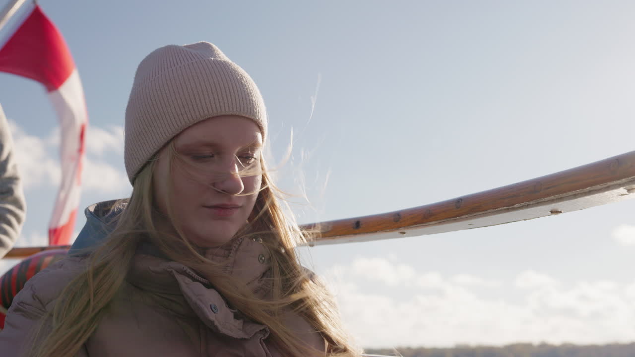 Dospívající dívka, pasažérka na lodi s měkkým slunečním svitem nad jezerem Ontario, mladá žena v teplém oblečení se dívá dolů v klidném, zamyšleném cestovním okamžiku.