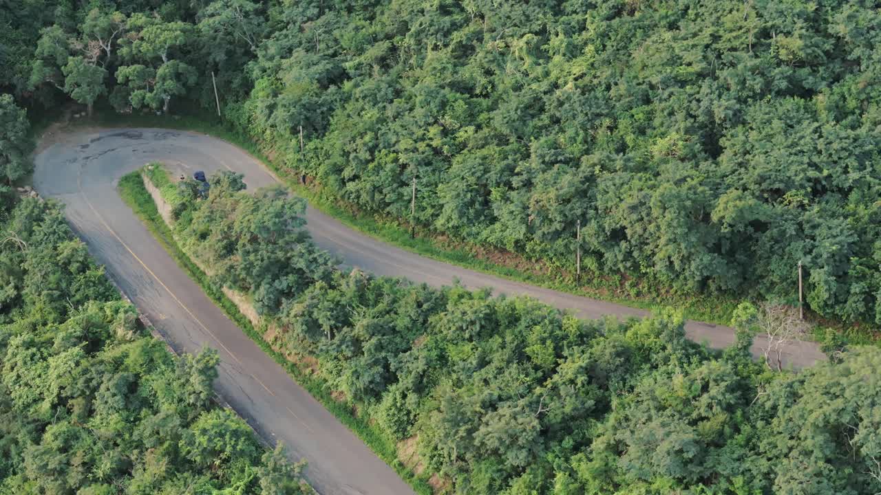 vista de avión no tripulado de una motocicleta subiendo por la carretera en zigzag en la ladera de la montaña verde
