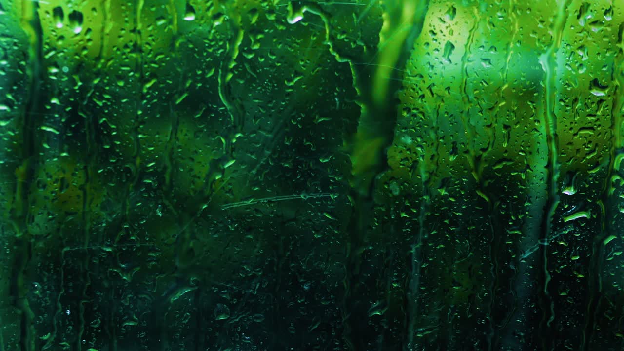 Heavy tropical rain outside the window, the climate is changing, the background of drops on the glass is green, the texture of a drop of water