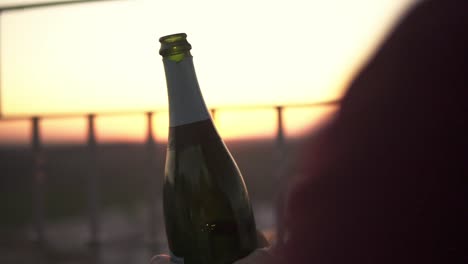 slowmotion shot of a man opening a bottle of prosecco with the sun setting