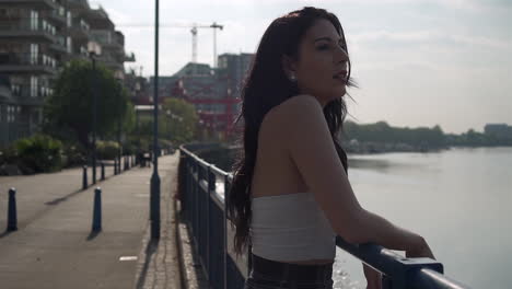 hermosa mujer latina de vacaciones apoyada en la barandilla, mirando el río támesis en londres, luego girando hacia la cámara, sonriendo y vagando