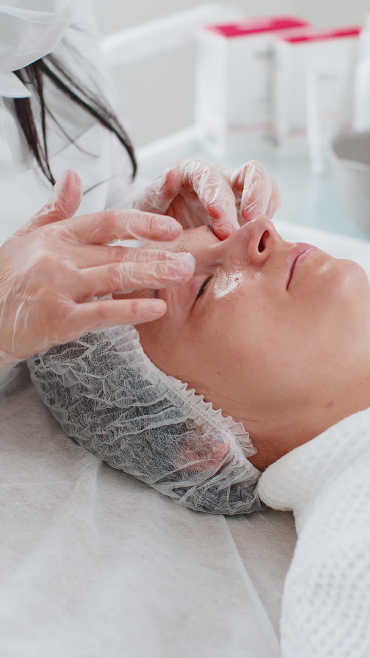 Terapista di cosmetologia che esegue un massaggio viso rilassante in una spa per una donna, con le mani, presso un salone detox e di benessere