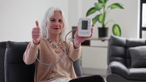 senior woman showing blood pressure monitor with thumbs up