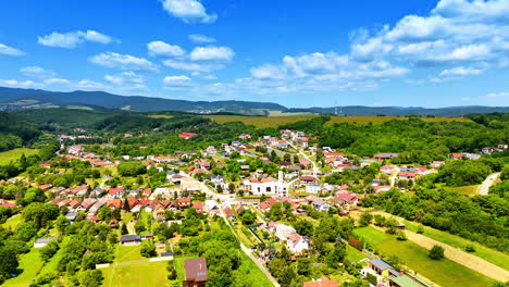 tranquil village in greenery. aerial view of a picturesque village with houses nestled amid lush hills and vibrant fields under a bright blue sky