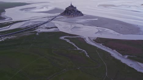 Le-Mont-Saint-Michel-on-a-cloudy-day-at-low-tide,-aerial