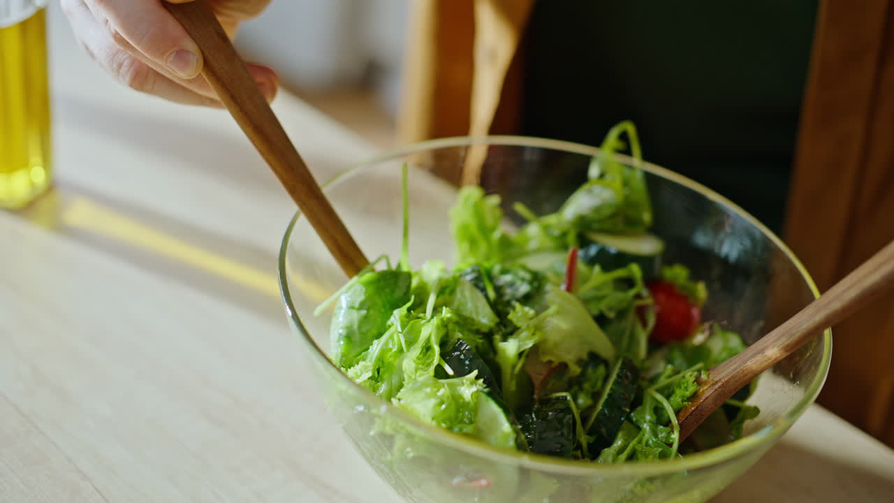 Nærbilde: Hender blander salat og tilbereder vegetarrett på kjøkkenet
