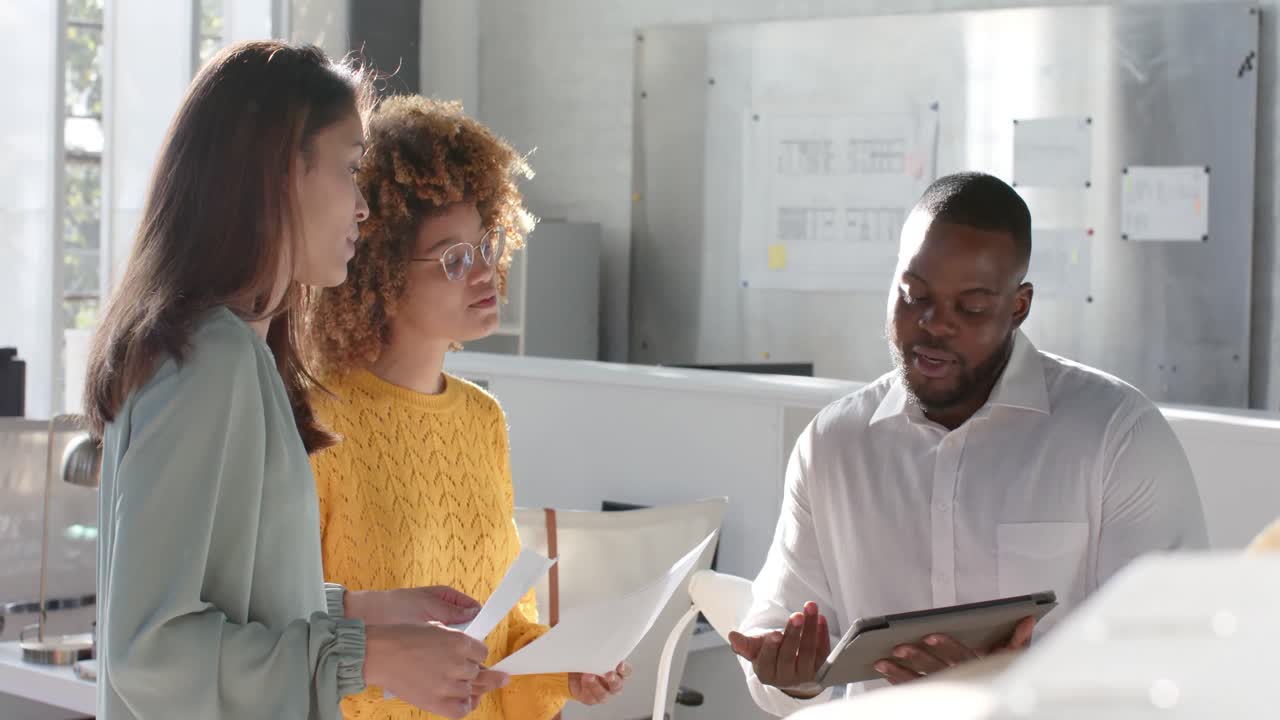 Diverse colleagues with documents and tablet discussing work in sunny office, slow motion