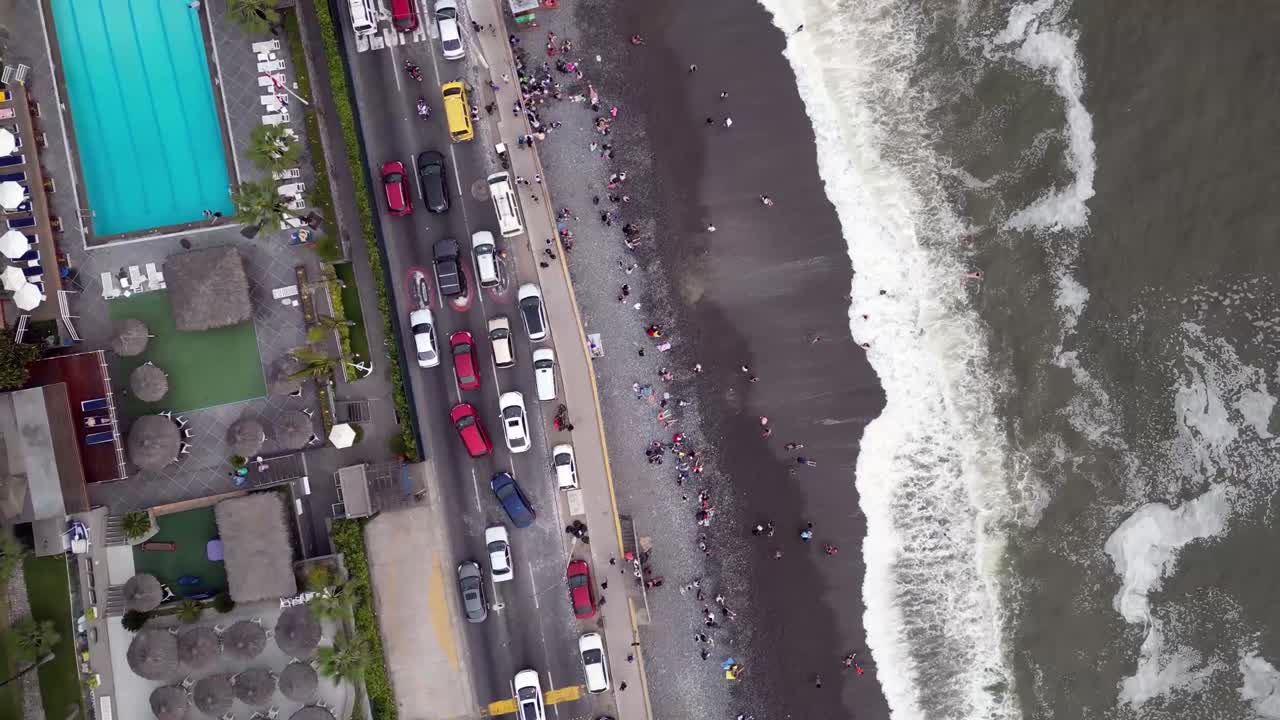 coches luchando en el atasco de tráfico en una calle costera de la ciudad sudamericana en frente de la playa donde las personas están nadando al lado de un club de piscina vacío
