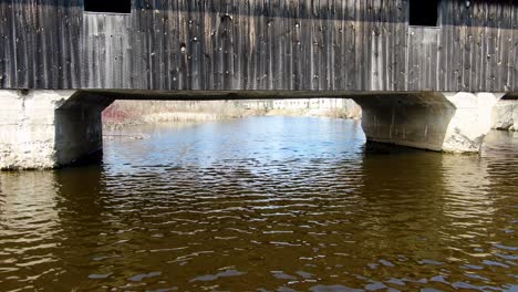 aerial fly-under the rustic covered wooden bridge over the creek in a small american town - dolly shot