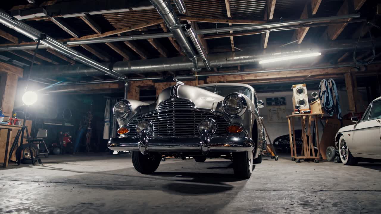 Aufnahme einer Oldtimer-Karosse aus einem niedrigen Winkel in einer schwach beleuchteten Garage, die ein nostalgisches und kinoreifes Video festhält