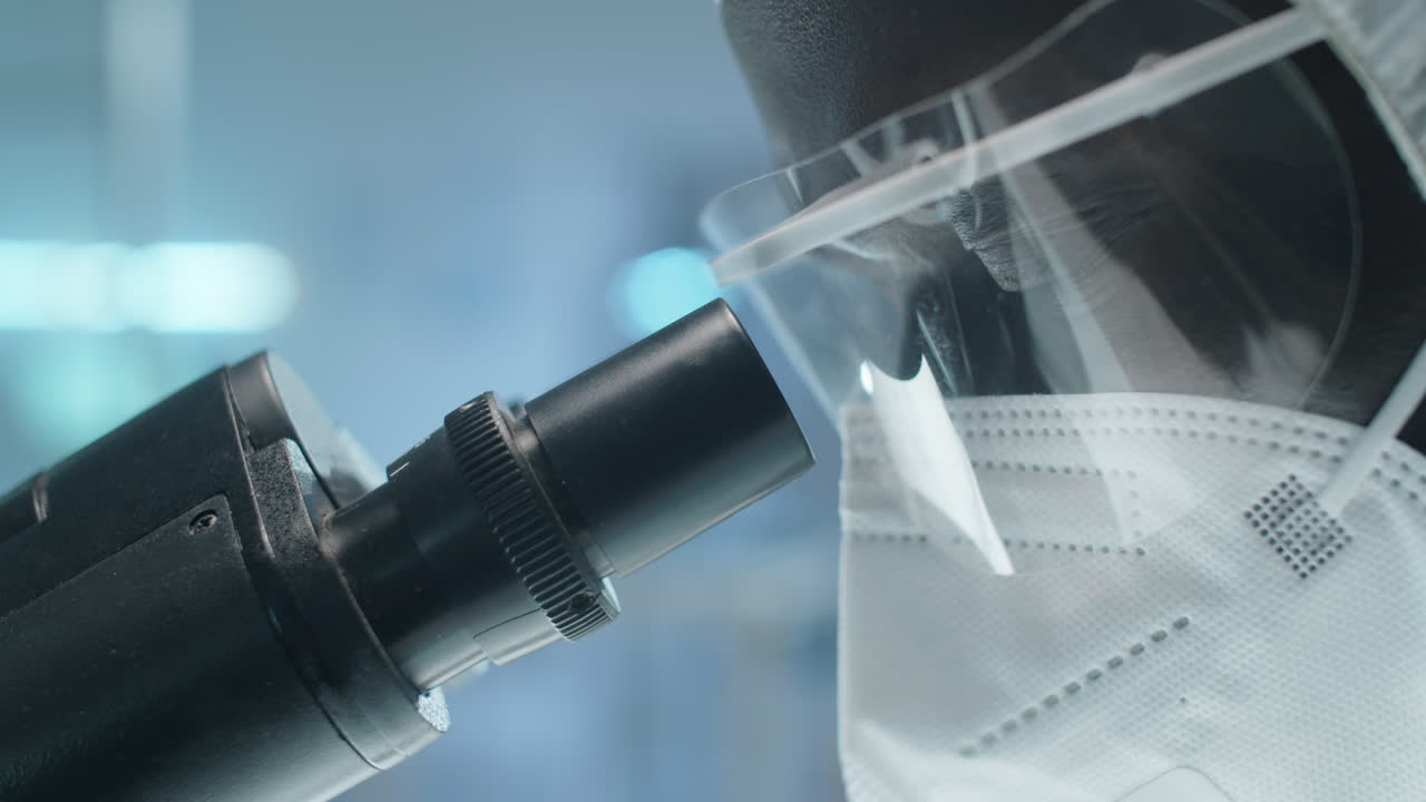 保護制服を着た黒い研究室の科学者が ⁇ 微鏡を使っています