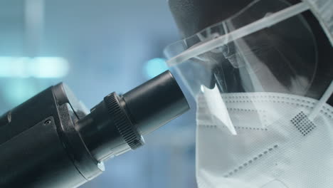 black lab scientist in protective uniform using microscope