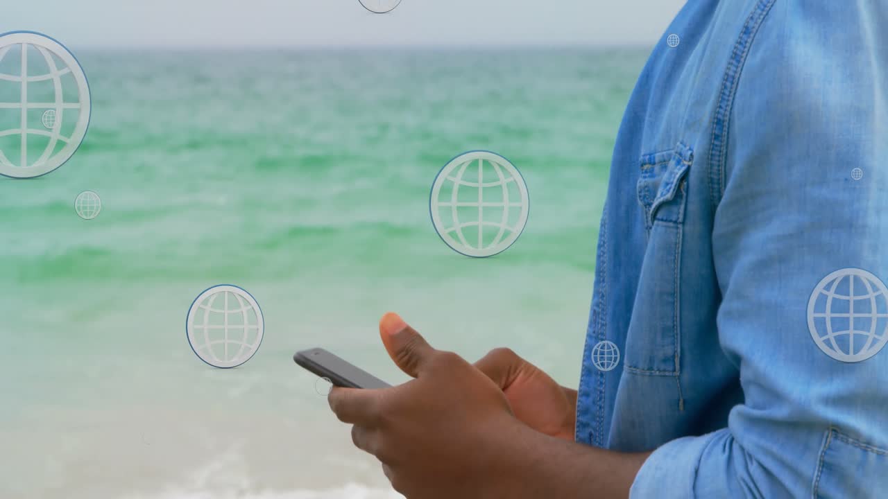 animación de globos sobre la sección media de un hombre afroamericano que usa un teléfono inteligente en la playa