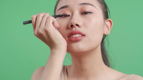 스튜디오에서 녹색 화면 배경에 서 있는 동안 완벽한 눈 화살을 하고 미소 짓는 아시아 여성의 클로즈업