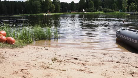 Pile-of-buoys-stacked-on-sandy-lake-shoreline-next-to-inflatable-boat-with-motor