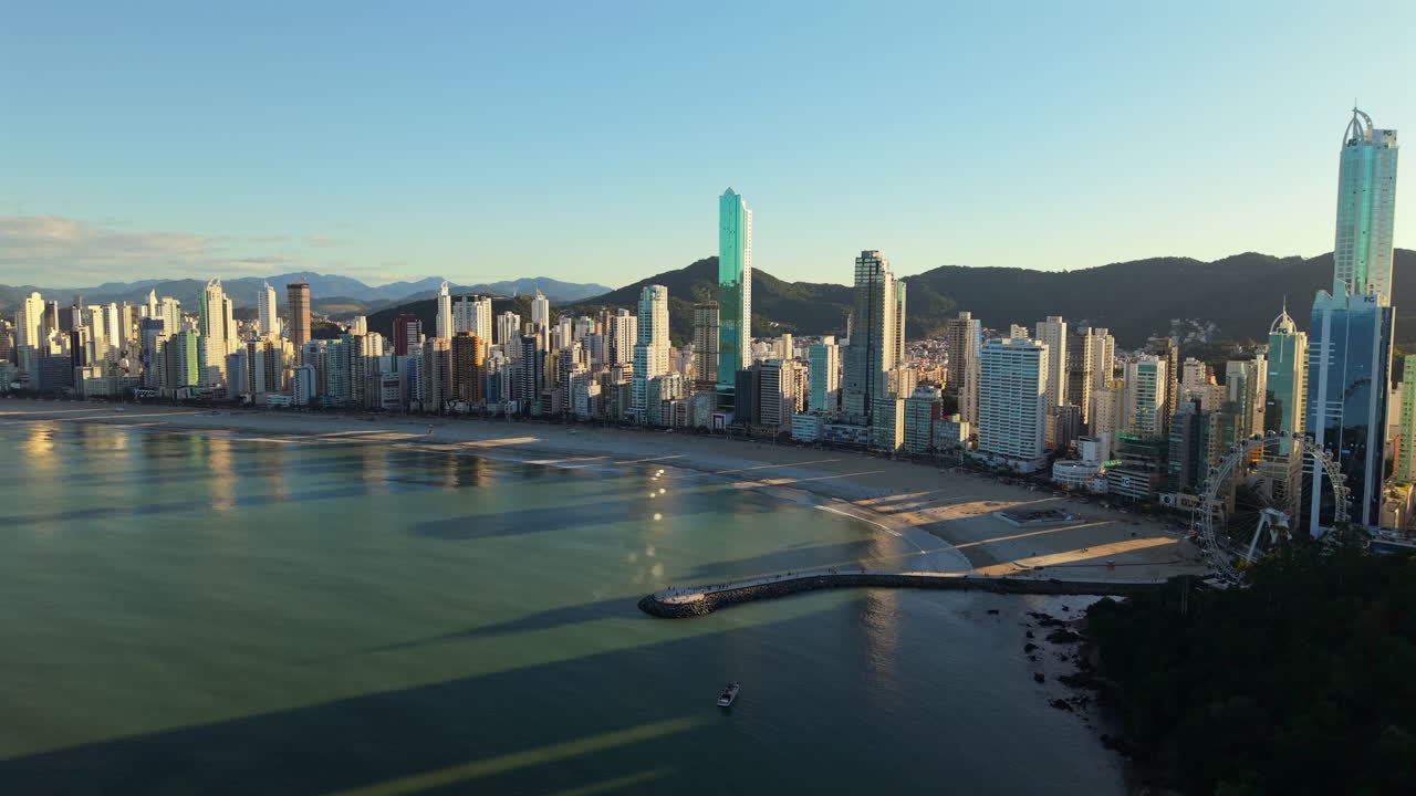 Aerial view of Balneario Camboriu skyline reflecting on the calm waters of the Atlantic Ocean during a beautiful sunrise, with mountains in the background