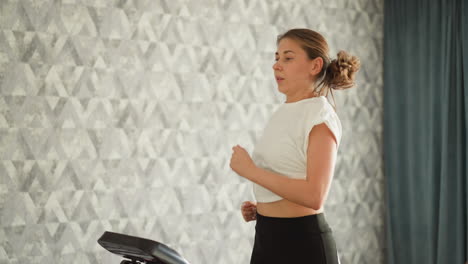 woman runs on treadmill at home. concentrated lady does hard cardio workout with automatic machine in house. athlete reduces stress by exercising